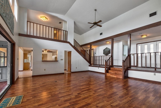unfurnished living room with ceiling fan, wood finished floors, stairway, and high vaulted ceiling