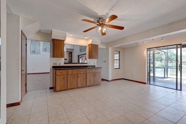 kitchen with baseboards, a sink, ceiling fan, and dark countertops