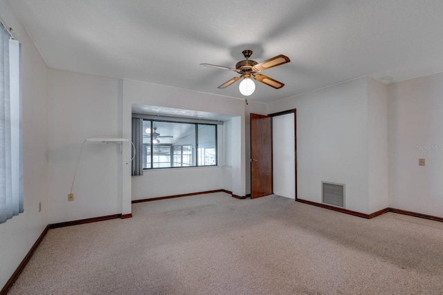 carpeted spare room featuring baseboards, ceiling fan, and visible vents