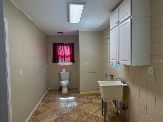 bathroom featuring toilet, baseboards, ornamental molding, and a wealth of natural light