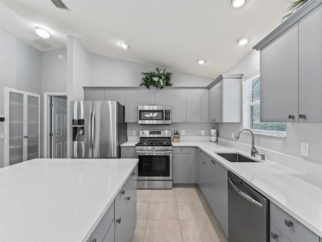 kitchen with lofted ceiling, light tile patterned flooring, gray cabinets, a sink, and stainless steel appliances