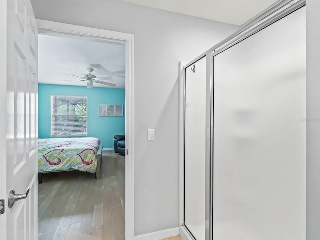bathroom with ceiling fan, a shower stall, wood finished floors, baseboards, and ensuite bathroom