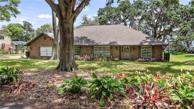ranch-style house featuring a chimney, a front yard, and brick siding