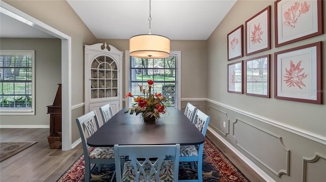 dining area with a wainscoted wall, wood finished floors, and lofted ceiling