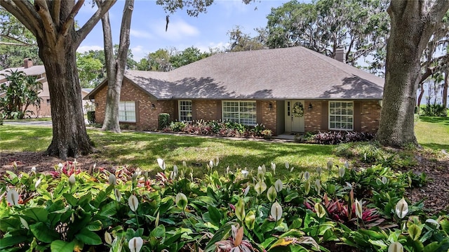 single story home with brick siding, a shingled roof, a front lawn, and a chimney