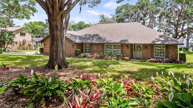 ranch-style home with brick siding, roof with shingles, and a front lawn