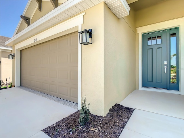 view of exterior entry featuring stucco siding, a garage, and concrete driveway