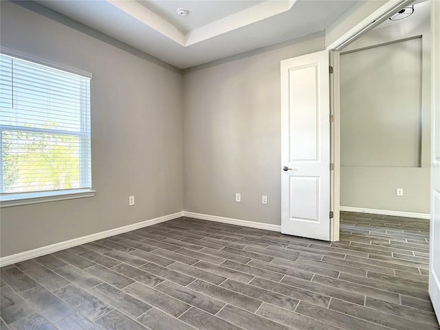 empty room with baseboards, dark wood finished floors, a tray ceiling, and a smoke detector