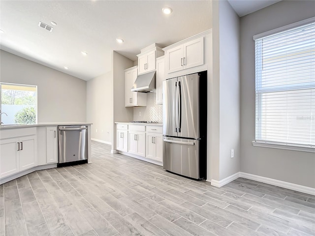 kitchen with appliances with stainless steel finishes, under cabinet range hood, light wood-style floors, white cabinets, and baseboards