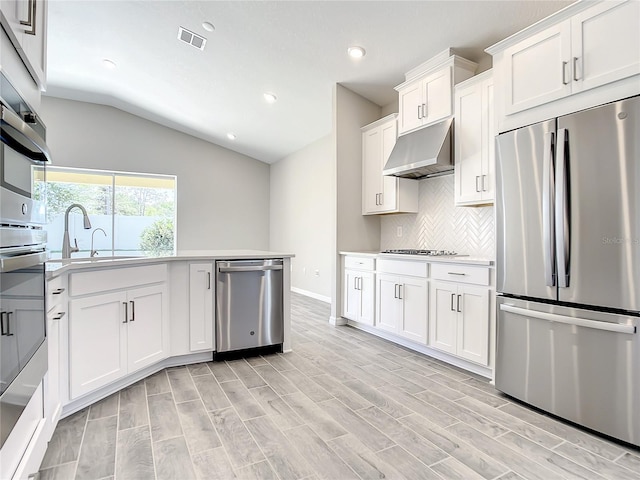 kitchen featuring stainless steel appliances, under cabinet range hood, vaulted ceiling, tasteful backsplash, and recessed lighting