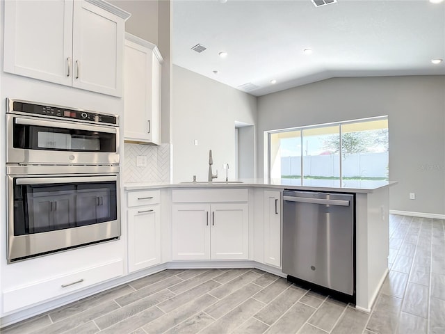 kitchen with appliances with stainless steel finishes, a sink, light countertops, wood finish floors, and lofted ceiling