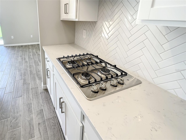 kitchen with stainless steel gas stovetop, light wood finished floors, tasteful backsplash, light stone countertops, and white cabinets