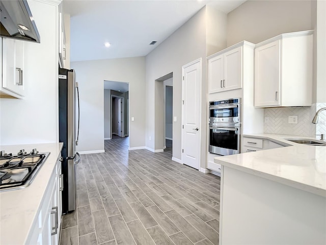 kitchen with a sink, under cabinet range hood, appliances with stainless steel finishes, white cabinets, and baseboards