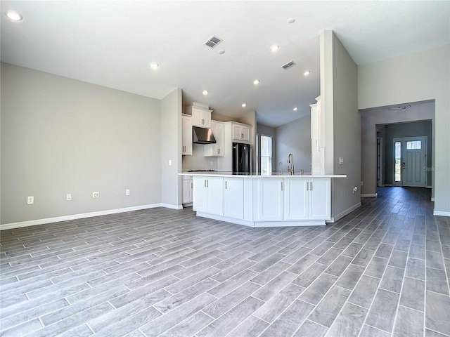 kitchen with refrigerator, under cabinet range hood, open floor plan, a sink, and vaulted ceiling