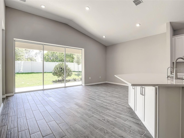 unfurnished living room with lofted ceiling, baseboards, recessed lighting, wood finished floors, and a sink
