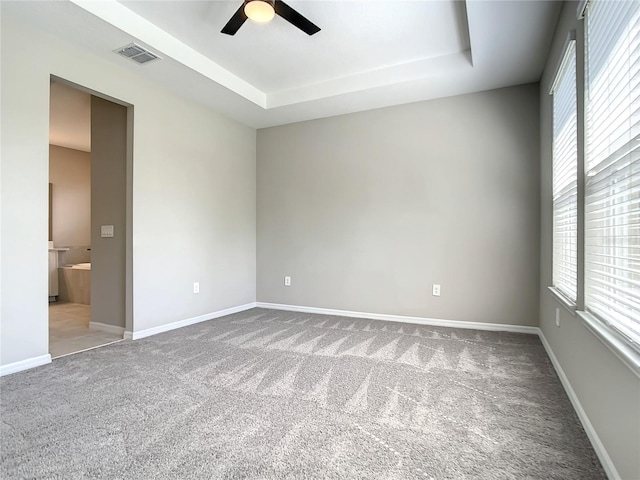 carpeted spare room featuring a ceiling fan, plenty of natural light, and a tray ceiling