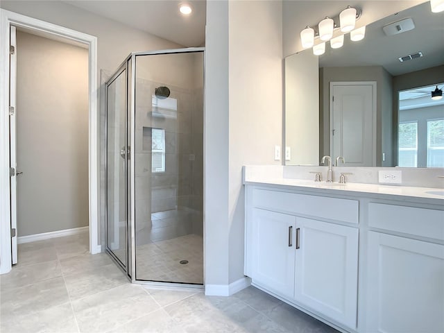 bathroom with a stall shower, baseboards, double vanity, ceiling fan, and tile patterned flooring