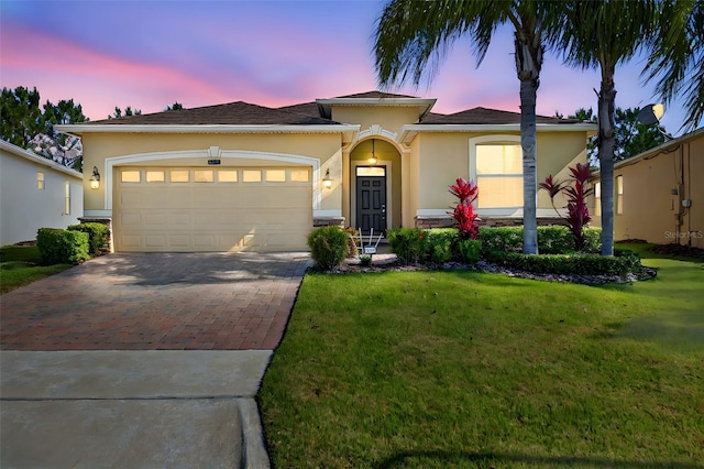 view of front of house featuring a garage, decorative driveway, stucco siding, and a front yard