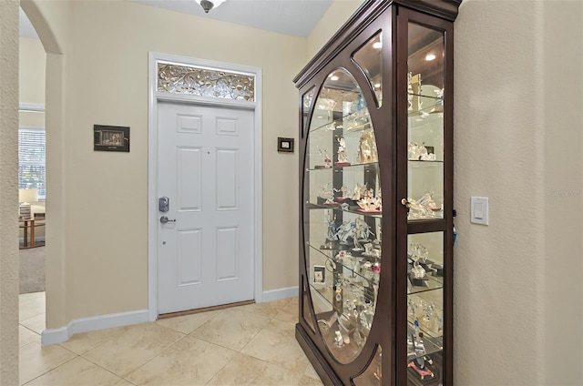 entryway with light tile patterned flooring, arched walkways, and baseboards