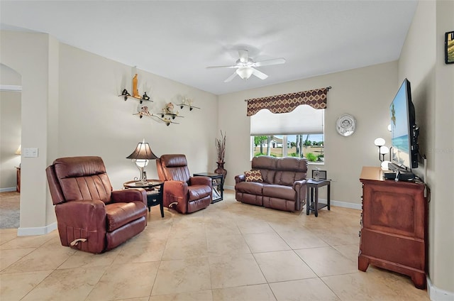 living room featuring arched walkways, baseboards, light tile patterned floors, and ceiling fan