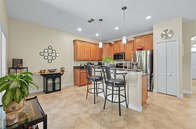 kitchen with a breakfast bar, dark countertops, stainless steel appliances, a kitchen island with sink, and visible vents