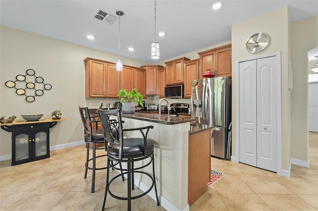 kitchen with a kitchen island with sink, a breakfast bar area, visible vents, hanging light fixtures, and appliances with stainless steel finishes