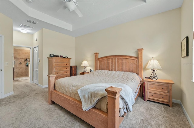 bedroom featuring light colored carpet, ensuite bath, visible vents, a raised ceiling, and baseboards