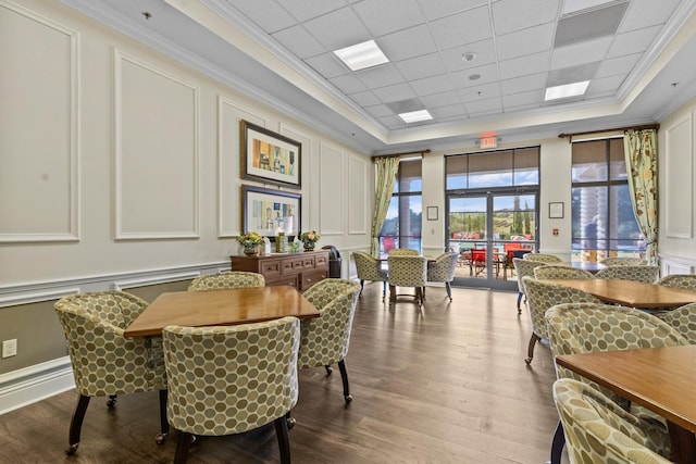 dining area featuring a tray ceiling, crown molding, a decorative wall, and wood finished floors