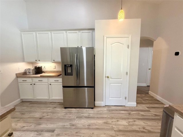 kitchen featuring stainless steel fridge, arched walkways, white cabinetry, light wood finished floors, and baseboards
