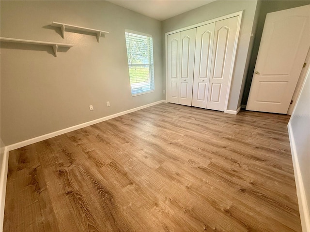unfurnished bedroom featuring wood finished floors, baseboards, and a closet