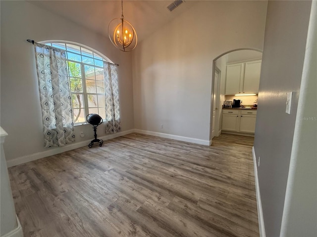 unfurnished dining area featuring arched walkways, wood finished floors, a chandelier, baseboards, and lofted ceiling