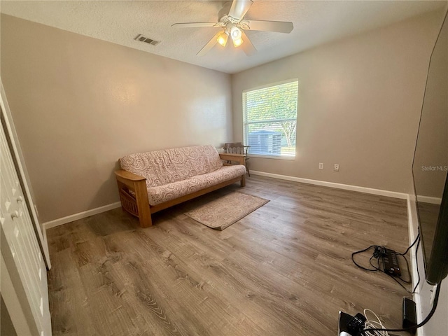 living area with wood finished floors, a ceiling fan, baseboards, and a textured ceiling