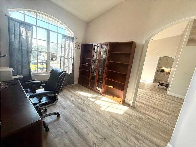 office with arched walkways, wood finished floors, lofted ceiling, and baseboards
