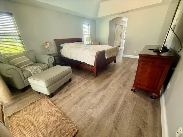 bedroom featuring arched walkways, light wood-style flooring, and baseboards