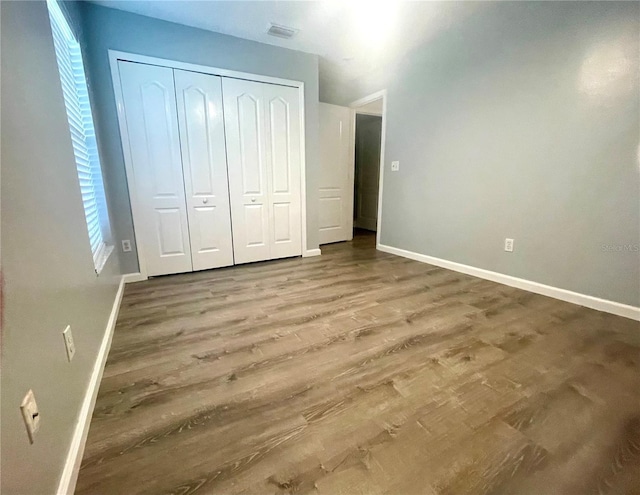 unfurnished bedroom with baseboards, wood finished floors, and a closet