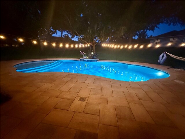 pool at night featuring a patio