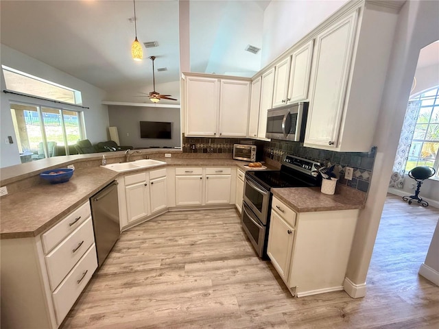 kitchen with appliances with stainless steel finishes, a sink, light wood-style floors, a ceiling fan, and backsplash