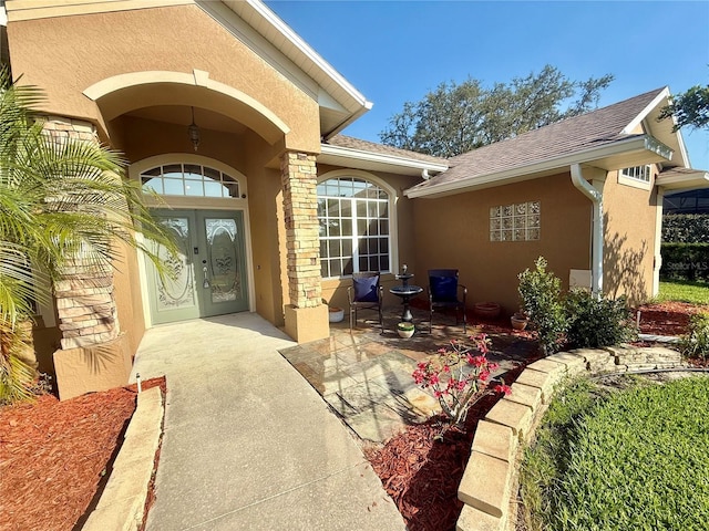 property entrance with stucco siding, roof with shingles, and french doors