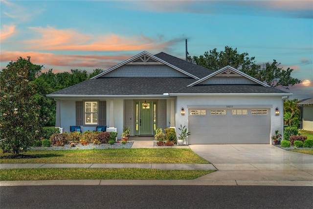 craftsman house with driveway, a front lawn, an attached garage, a shingled roof, and stucco siding