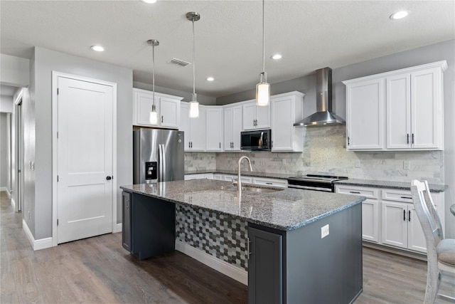kitchen with appliances with stainless steel finishes, a sink, wall chimney exhaust hood, wood finished floors, and tasteful backsplash