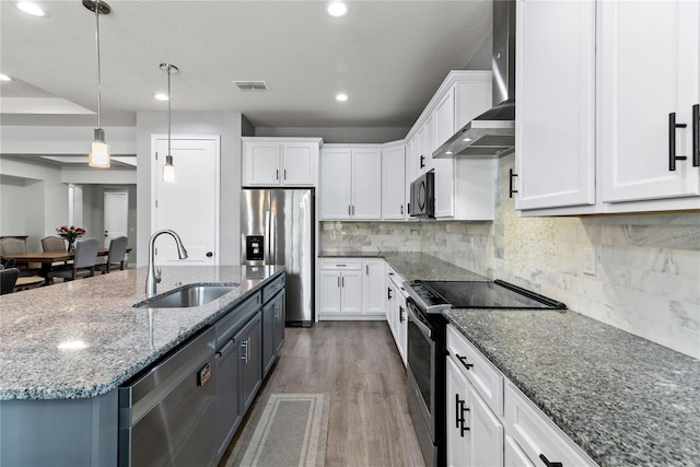 kitchen featuring wood finished floors, wall chimney range hood, white cabinetry, a sink, and appliances with stainless steel finishes