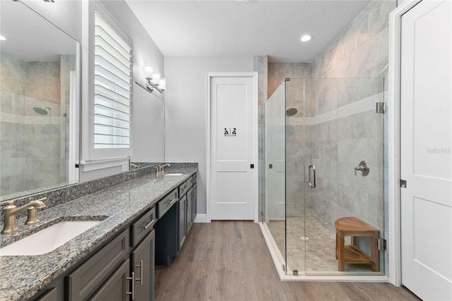 full bath with a sink, double vanity, a shower stall, and wood finished floors