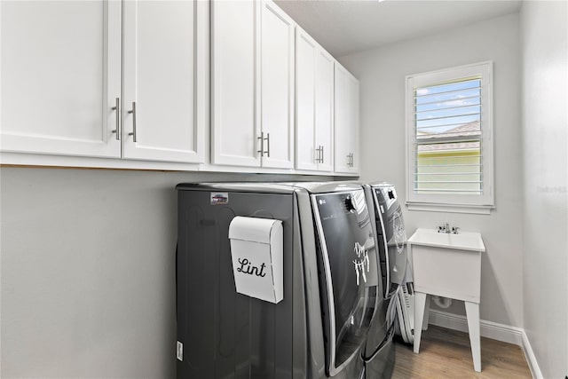 clothes washing area with baseboards, wood finished floors, cabinet space, and washing machine and clothes dryer