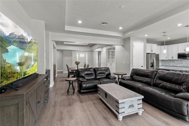 living area featuring a textured ceiling, light wood-style flooring, recessed lighting, baseboards, and a tray ceiling