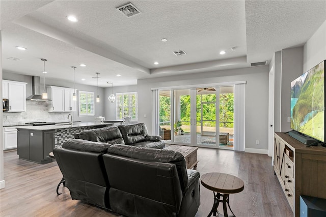 living room with visible vents, baseboards, light wood-type flooring, a textured ceiling, and a tray ceiling