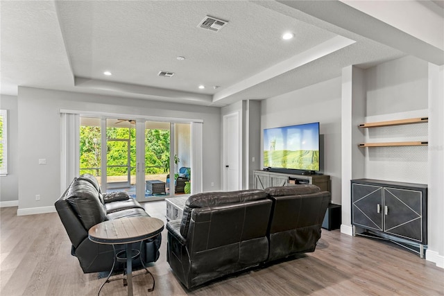 living area with visible vents, wood finished floors, baseboards, a textured ceiling, and a tray ceiling