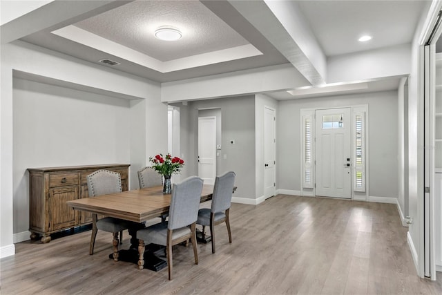 dining room with baseboards, a raised ceiling, light wood-style flooring, and visible vents