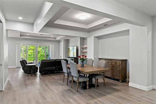 dining space featuring a raised ceiling, baseboards, visible vents, and light wood finished floors