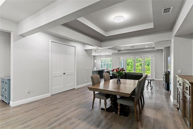 dining space featuring visible vents, wood finished floors, baseboards, a textured ceiling, and a raised ceiling