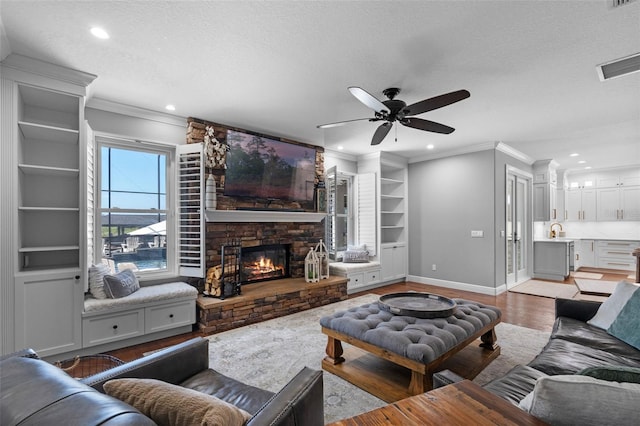 living room featuring ceiling fan, a stone fireplace, visible vents, crown molding, and light wood-type flooring